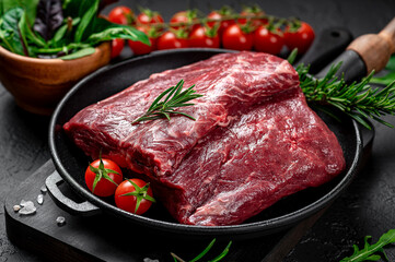 Raw organic marbled beef with spices on a wooden cutting board on a black slate, stone or concrete background.