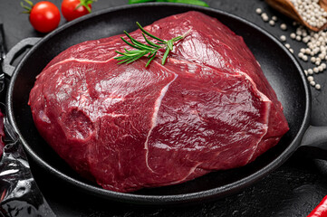 Raw organic marbled beef with spices on a wooden cutting board on a black slate, stone or concrete background.