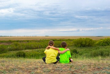 Naklejka na ściany i meble Two children sitting in the steppe with their backs. High quality photo