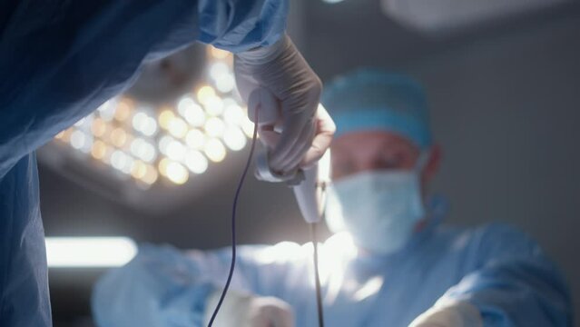 Adult male surgeon looks at monitor and operates patient with his colleagues. Professional medics use modern laparoscopy instruments during surgery in operating room. Medical staff at work in clinic.