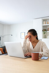 Vertical portrait of young Asian woman feeling tired and having headache after working long hours...