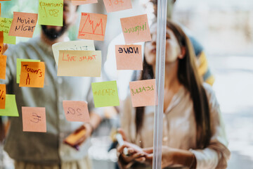 Multinational business team brainstorming, collaborating, and strategizing for successful projects. Creative people discussing goals, writing on adhesive notes over glass.