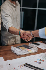 Multicultural colleagues bid farewell, embracing as one begins a new job. A touching moment of saying goodbye and shaking hands between business people indoors.