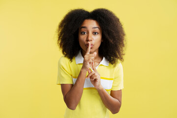Portrait excited smiling African American woman holding finger near mouth, showing silence gesture