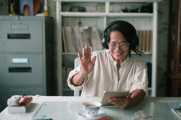 Smiling mature old woman holding using digital tablet sitting while online video call with friend or relative cousin at home living room. Internet information technology and lifestyle concept.