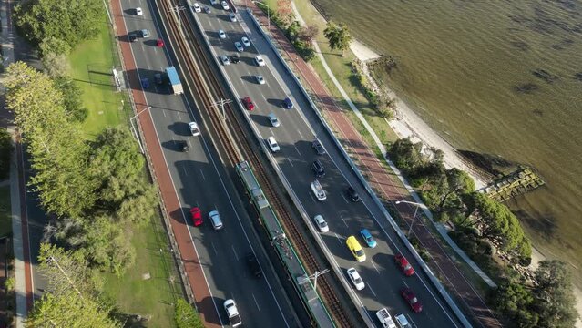 Aerial tilt up shot of high frequented highway beside Swan River in Perth City during sunny day, Western Australia

