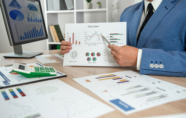 Business man in suit calculate annual profit by duty with finance document computrer and calculator