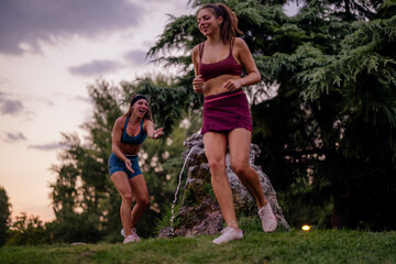 Fit girls having fun, splashing water in a park. Active and attractive athletes, with athletic bodies. Happy and healthy, enjoying outdoor sport and exercise.