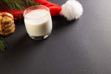Obraz na płótnie Canvas Glass of milk, christmas cookies and santa hat with copy space on black background