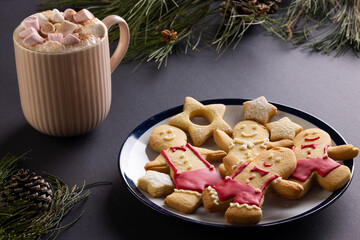 Mug of chocolate with marshmallows, plate of christmas cookies and copy space on black background