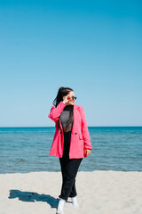 Woman in casual clothes, pink jacket and sunglasses on the seashore