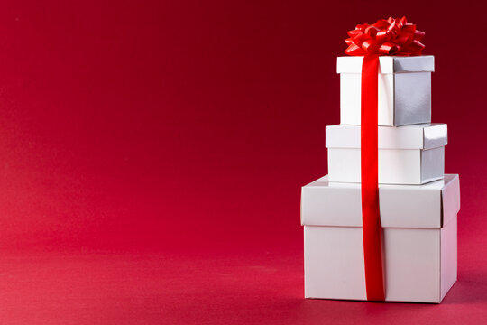 Stack of white christmas presents with red ribbon and copy space on red background