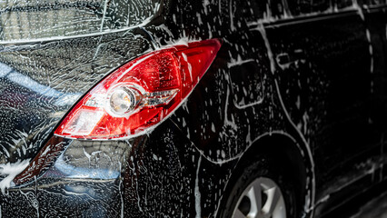 Soup foam covering on black car body and tail light. Self service car wash cleaning process. Car...