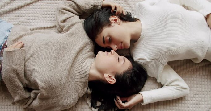 Top view on couple of lesbian woman in love, lying on bed touching and stroking hair each other tender. Romantic relationship, closeness and affectionate between two attractive girls