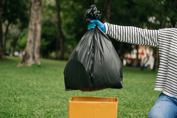 Hand holding garbage black bag putting in to trash to clean. Clearing, pollution, ecology and plastic concept..