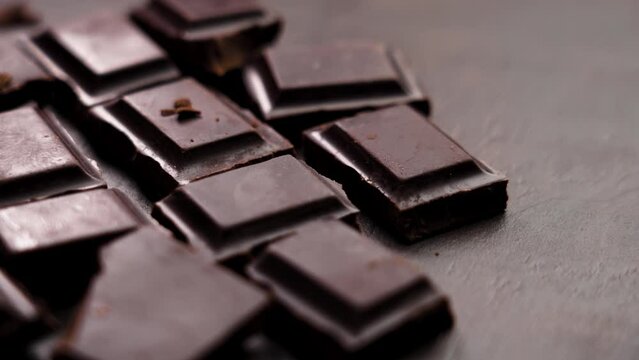 Closeup of pieces of broken dark bitter chocolate bar on a brown board. Rotation