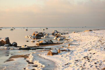 A view of the snow-covered Baltic sea coast at sunset. Stones in the water close-up. Idyllic winter...