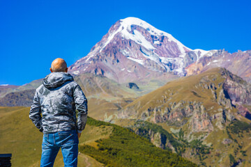 Naklejka na ściany i meble traveler enjoys the picturesque view of Mount Kazbek against the blue sky. Travel in Georgia