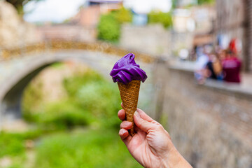 A hand holds a wine ice cream cone on a blurred background of the old city of Tbilisi. Wine ice cream in a waffle cone.