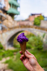 A hand holds a wine ice cream cone on a blurred background of the old city of Tbilisi. Wine ice cream in a waffle cone.