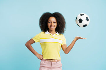 Confident African American woman with curly hair holding soccer ball looking at camera