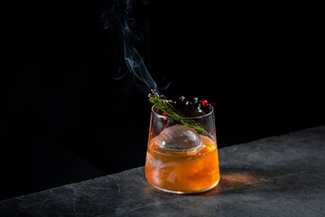 aromatic cocktail with a sprig of pine needles and round ice on a dark background, side view