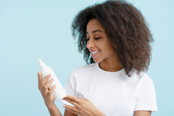 Authentic happy african american woman with curly hair holding shampoo bottle reading description