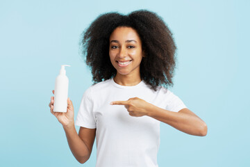 African american woman with curly hair in white t shirt holding bottle mockup pointing finger