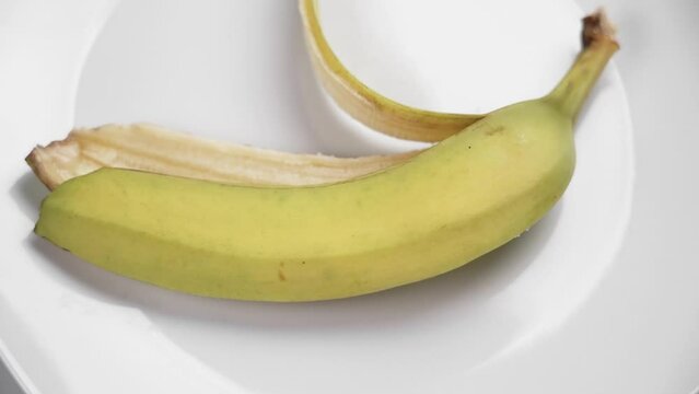 Throwing a yellow banana peel on a white ceramic plate close up