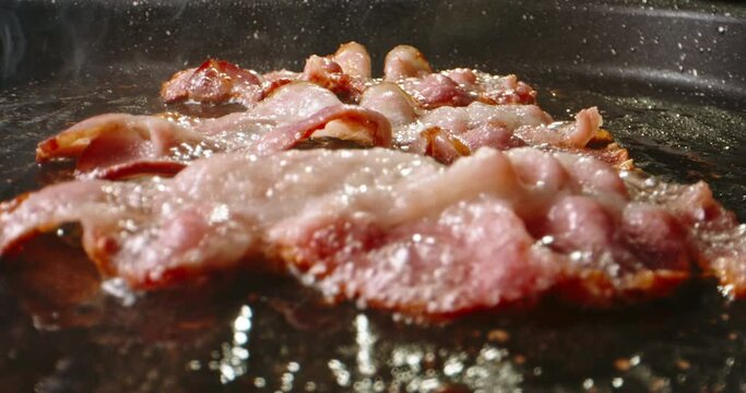 Frying halal beef bacon in pan side view close up slow motion. Pan-fried bacon slices capture the essence of sizzling goodness, ready to be devoured with delight. Traditional breakfast with bacon. Fat