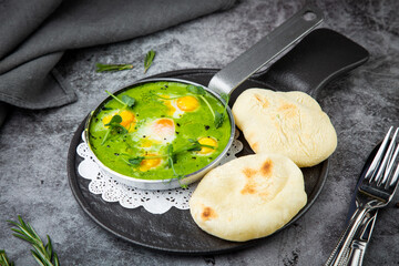green broccoli soup with egg and herbs in a frying pan with flatbread, side view