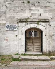 Fototapeta na wymiar Arched entrance with open green metal door in brick stone wall leading to 16th century Atik Valide Mosque in Uskudar district, Istanbul, Turkey