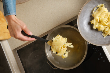 Top view of female hand taking cooked pasta out of the saucepan