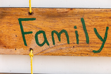 Family inscriptions in green paints on a wooden board suspended on yellow rope. Family concept, wedding gift, celebration day sign.Signboard for a photo shoot.Handmade for people in love, inspiration.