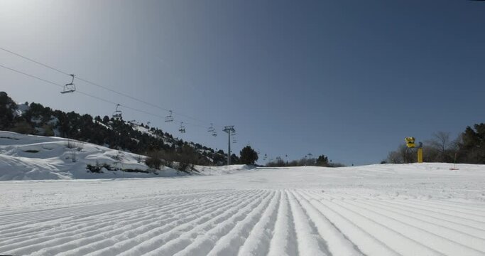 Velvet snow, working cable cars. Winter holidays at ski resort. Velvet ski snow illuminated by morning frosty sun. Tourists climb to starting point of descent on ski lift. Close up velvet slope snow