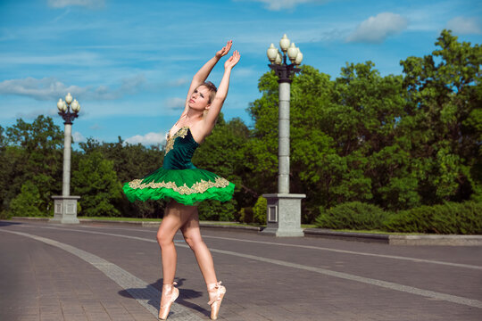 One Winsome Professional Caucasian Ballet Dancer in Green Tutu Dress Posing in Standing Position With Lifted Hands Against Blue Sky