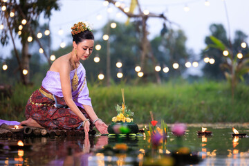 Loi Krathong Festival, Thai woman holding a krathong sitting on a raft by the river, Asian women in traditional Thai costumes bring krathongs to float on Loi Krathong Day, - obrazy, fototapety, plakaty
