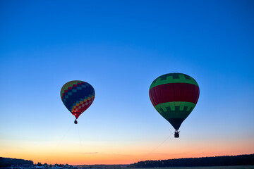Fototapeta na wymiar Colorful Air Balloons Levitating Over the Field Outdoors Against Clear Blue Skies At Twilight.