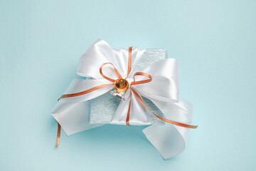 Gift box wrapped in blue silver paper with white and gold ribbon bow and bells. Blue background, top view. Christmas and New Year gifts, Boxing Day.