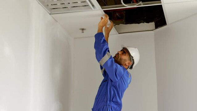 Handsome caucasian electrician man wearing safety workwear checking and repairing Maintenance light bulbs, wiring and fire sprinkler in the ceiling. Install the lighting system in the ceiling in room.