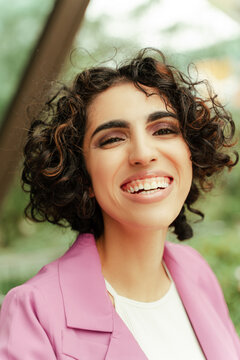 Portrait of curly middle eastern woman wearing pink outfit posing on the street