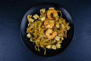 Black plate with pad thai on a slate board. Top view