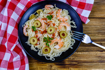 Italian pasta with shrimps and olives in a black plate. Top view