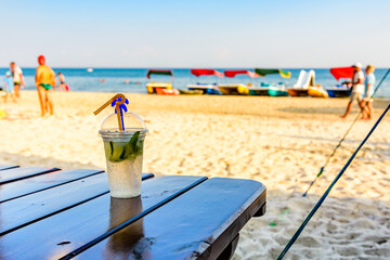 Mojito cocktail on wooden table with sandy beach on a background