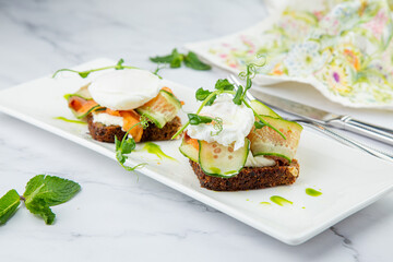 canapes on black bread with cheese, red fish, herbs and cucumber side view