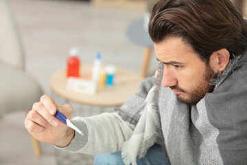 man with cold sitting on sofa with thermometer