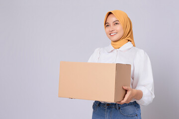 Smiling friendly Asian Muslim Woman in white shirt holding package box and looking aside isolated on white background. Shopping and delivery concept