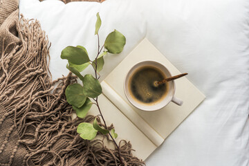 Draufsicht auf einem Tasse Kaffee und ein Buch auf einer weißen Bettdecke. Frühstück, Heißgetränk.