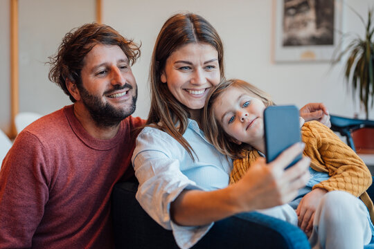 Happy woman taking selfie through smart phone with family at home