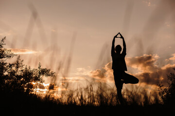 Silhouette woman practicing tree pose yoga at sunset